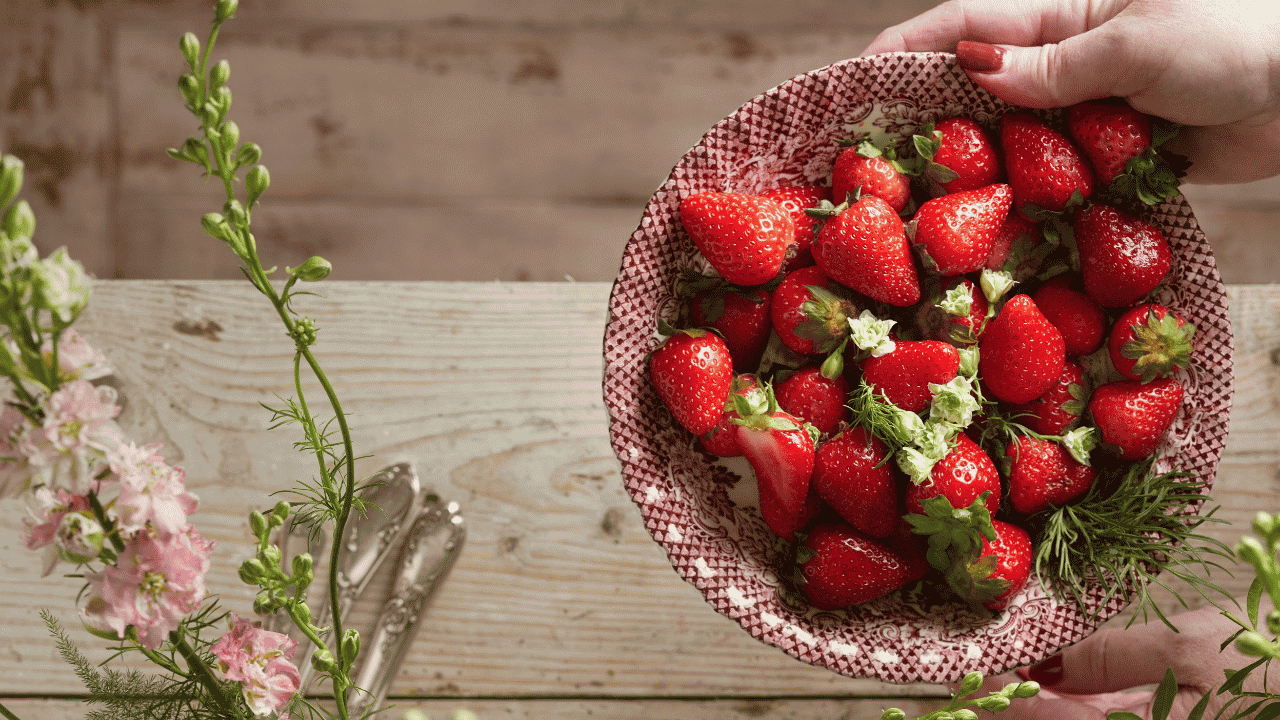 Person holding a bowl full of strawberries on a wooden table top