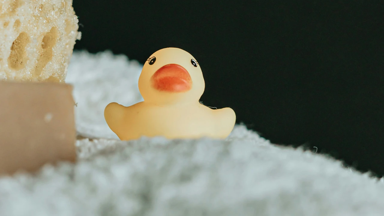 Patito de goma en una toalla de baño junto con esponja y jabón